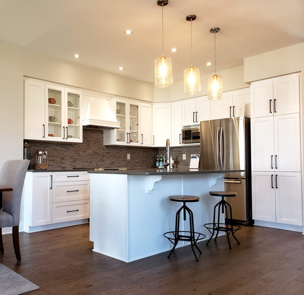 Full view of a renovated kitchen plan with new cupboards and mosaic tiled backsplash, hardwood floor