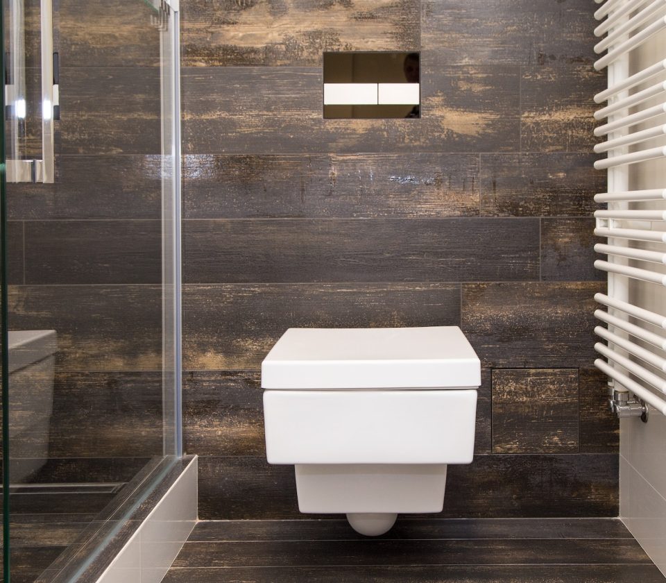 A modern wall-mounted compact square-shaped toilet in a brown tiled bathtub